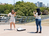 shutterstock_2429201687_tourist taking picture of street violinist_tūrists bildē ielas muzikanti.jpg
