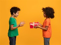 shutterstock_2458596035_boy giving gift to friend_zēns dāvina dāvanu draugam.jpg